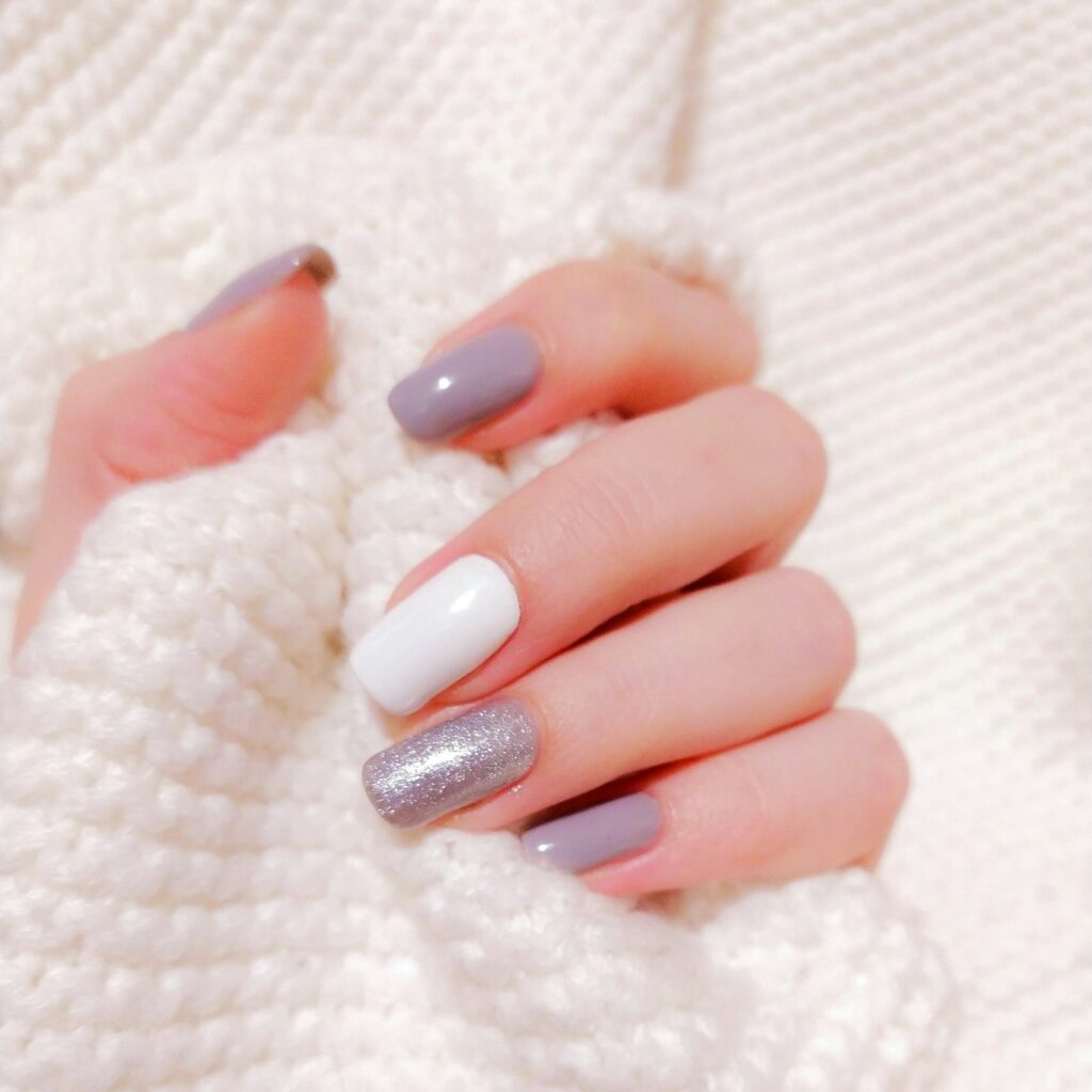 Hand met mauve, witte en zilveren glitternagels op een witte gebreide trui